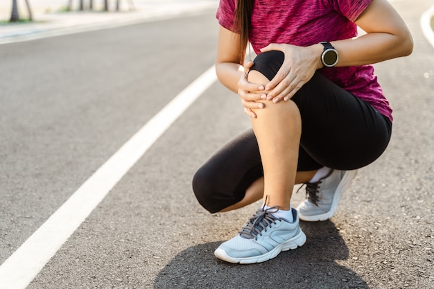 Knieverletzungen. Sportfrau mit starken athletischen Beinen, die Knie mit ihren Händen im Schmerz halten, nachdem sie Muskelverletzung während eines Lauftrainingstrainings auf der Laufbahn erlitten haben. Gesundheits- und Sportkonzept.