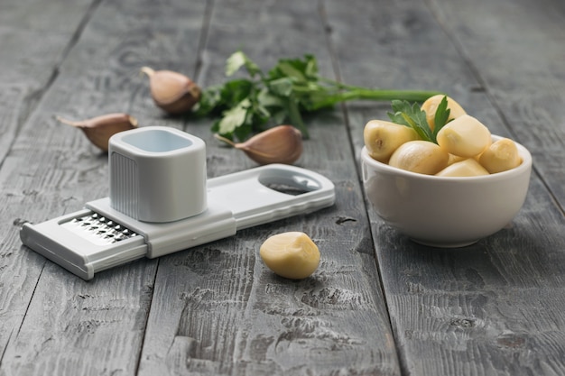 Knoblauch in einer weißen Schüssel und Handreibe auf einem Holztisch