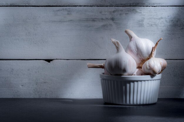 Knoblauch in weißer Schüssel auf Holzhintergrund. Weißes Themenkonzept.