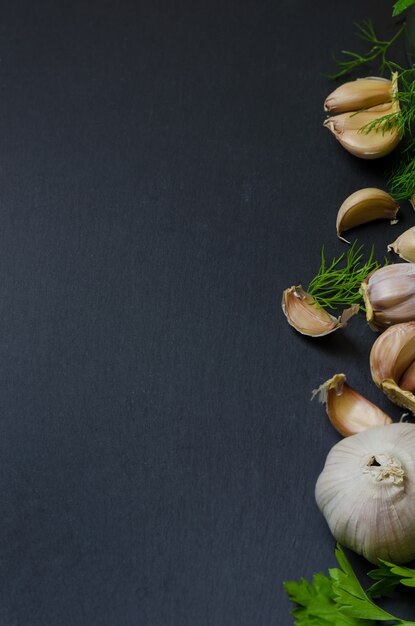 Knoblauch mit Dill und Petersilie auf dunklem Hintergrund.