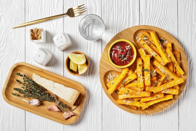 Knoblauch-Parmesan-Polenta-Pommes mit Parmesan-Käse, Thymian und Gewürzen in einem Bambusgericht mit Tomatensauce auf einem weißen Holztisch, flache Lage, italienische Küche