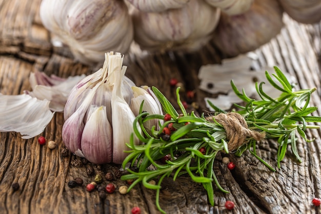 Knoblauchzehenknolle mit frischem Rosmarin und Gewürzen auf altem Holztisch.