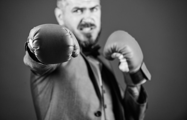 Knockout y energía Pele a un hombre de negocios con traje formal y corbata de moño Éxito en los negocios y el deporte poderoso boxeador listo para la batalla corporativa hombre barbudo con guantes de boxeo golpeando sin dolor no hay ganancia