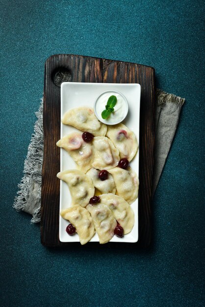 Knödel mit Kirsche und Sauerkreme auf einem weißen quadratischen Teller Freier Platz für Text auf einem dunklen Hintergrund