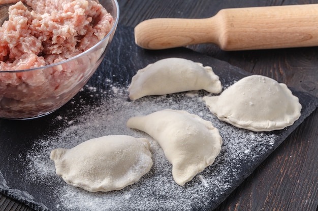 Knödel roh auf einem Holzbrett. Traditionelles hausgemachtes Essen. Der Prozess des Kochens Knödel. Traditionelle Pierogi, Pelmeni, Ravioli, Knödel mit Fleisch.