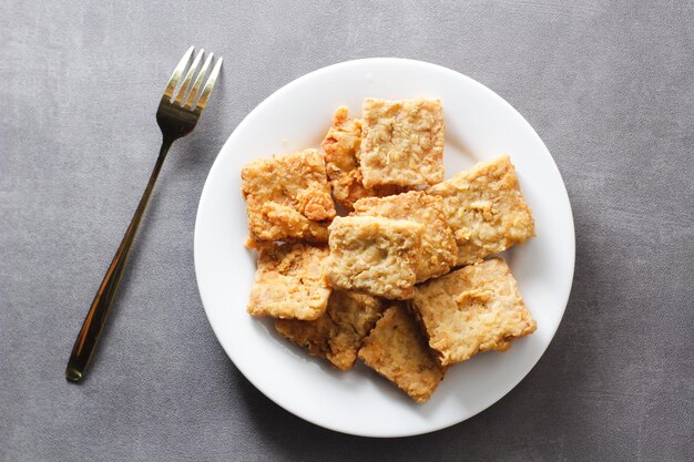 Knusprig gebratenes Tempeh auf einem weißen Teller mit grauem Hintergrund