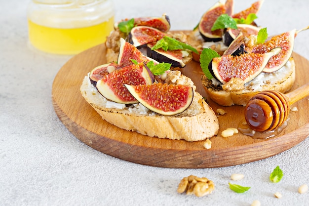 Knusprige Bruschetta mit weichem Ricotta, reifen Feigen, Walnüssen und Pinienkernen, Minze und Honig auf hellem Hintergrund.