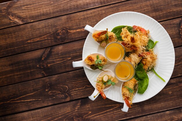 Knusprige Garnele in Kataifi-Kruste und Thymian mit Champagne Sauce in den Gläsern liegen auf einer weißen Platte auf einem waldigen Hintergrund. Freier Platz für Text