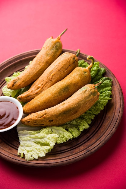 Knusprige Green Chilli Pakora oder Mirchi Bajji, serviert mit Tomatenketchup auf stimmungsvollem Hintergrund. Es ist ein beliebter Snack zur Teezeit aus Indien, besonders im Monsun. Selektiver Fokus