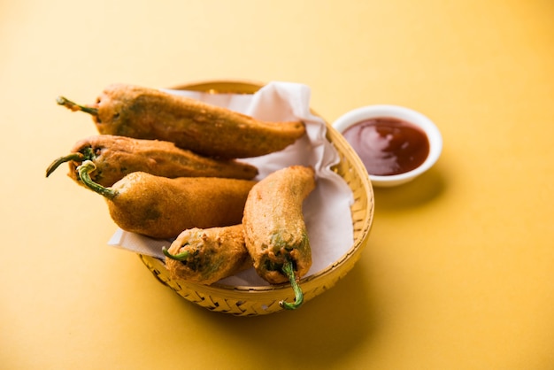 Knusprige Green Chilli Pakora oder Mirchi Bajji, serviert mit Tomatenketchup auf stimmungsvollem Hintergrund. Es ist ein beliebter Snack zur Teezeit aus Indien, besonders im Monsun. Selektiver Fokus