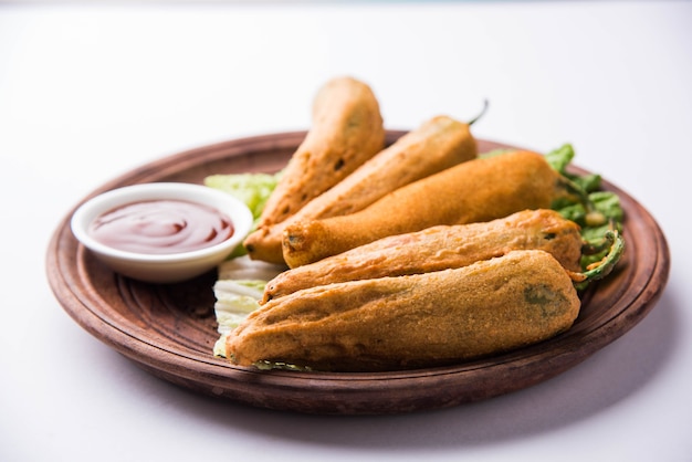 Knusprige Green Chilli Pakora oder Mirchi Bajji, serviert mit Tomatenketchup auf stimmungsvollem Hintergrund. Es ist ein beliebter Snack zur Teezeit aus Indien, besonders im Monsun. Selektiver Fokus