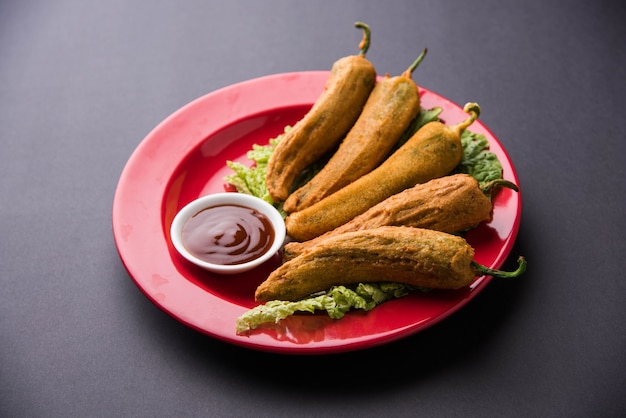 Knusprige Green Chilli Pakora oder Mirchi Bajji, serviert mit Tomatenketchup auf stimmungsvollem Hintergrund. Es ist ein beliebter Snack zur Teezeit aus Indien, besonders im Monsun. Selektiver Fokus