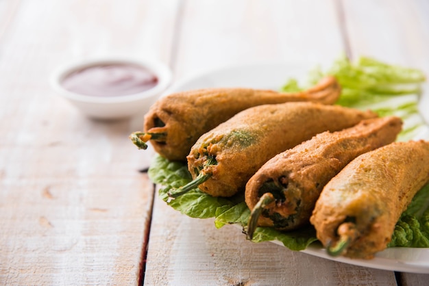 Knusprige Green Chilli Pakora oder Mirchi Bajji, serviert mit Tomatenketchup auf stimmungsvollem Hintergrund. Es ist ein beliebter Snack zur Teezeit aus Indien, besonders im Monsun. Selektiver Fokus