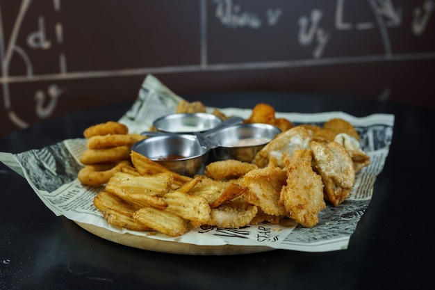 Knusprige Hühnernuggets mit gebratenen goldenen Kartoffelscheiben mit gebratenen Zwiebelringen, mit Käsesauce und Pilzsauce und mit Ketchup auf dem Tisch in einem Café. Snack zum Bier. Fast Food