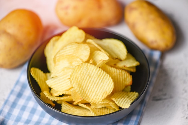 Knusprige Kartoffelchips auf dem Küchentisch und frische rohe Kartoffeln auf Holzhintergrund Kartoffelchips Snack auf Schüssel