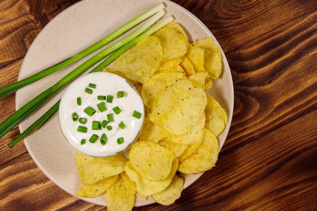 Knusprige Kartoffelchips mit Frühlingszwiebeln und Sauerrahm auf Holztisch. Ansicht von oben