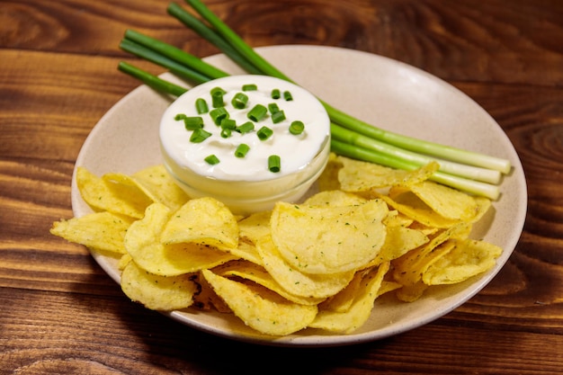 Knusprige Kartoffelchips mit Frühlingszwiebeln und Sauerrahm auf Holztisch