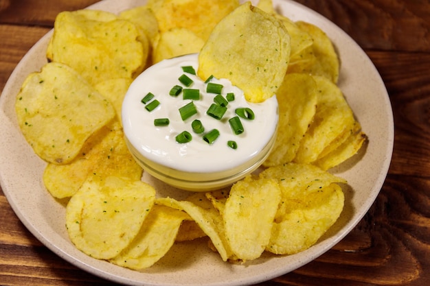 Knusprige Kartoffelchips mit Frühlingszwiebeln und Sauerrahm auf Holztisch