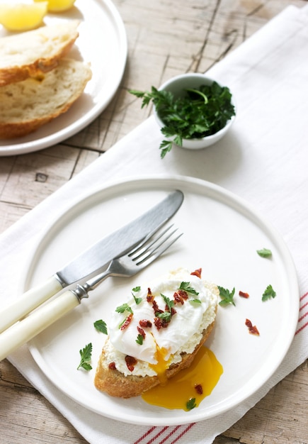 Knusprige Stangenbrottoast mit Hüttenkäse, poschiertem Ei und getrockneten Tomaten auf einem hellen Hintergrund.