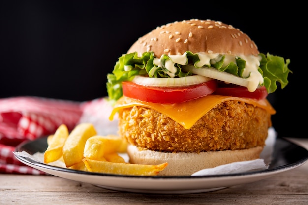 Knuspriger Hühnerburger mit Käse und Pommes Frites auf Holztisch