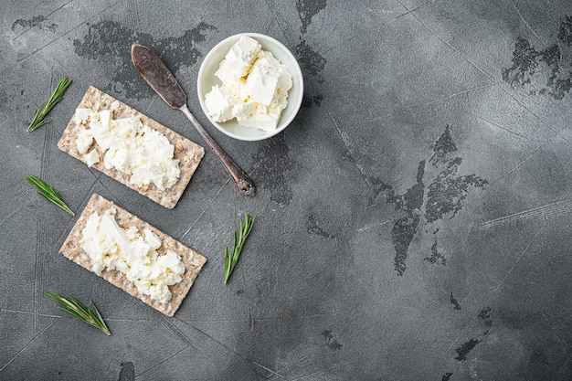 Knuspriges Brot mit Frischkäse-Set, auf grauem Steintischhintergrund, Draufsicht flach, mit Kopienraum für Text