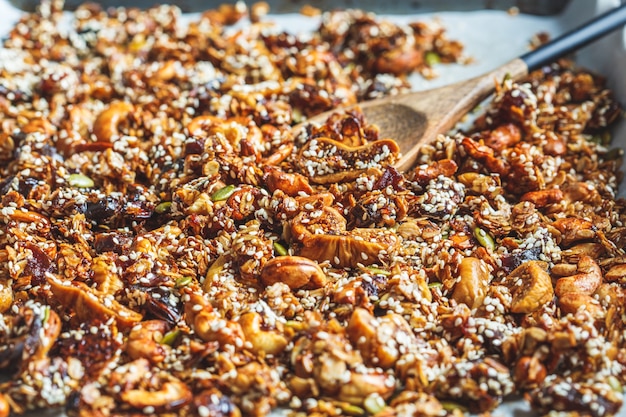 Knuspriges hausgemachtes Müsli mit Nüssen, getrockneten Früchten und Sesam auf einem Backblech.