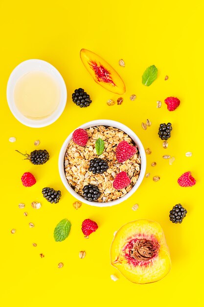 Knuspriges Müsli, Beeren und Minze in Keramikschale und Himbeeren, Brombeeren, Pfirsich und Honig.