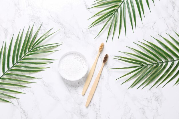 Öko-Bambuszahnbürsten und Zahnputzmittel mit Palmblättern auf Marmorhintergrund Zahnpflegekonzept