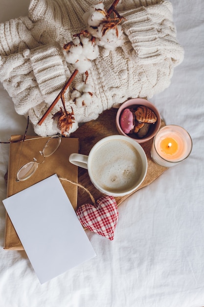 Öko-Dekor für zu Hause. Gemütliche Einrichtung zu Hause. Eine Tasse Cappuccino, Kekse, eine Kerze auf dem Bett. Wintermorgen. Ferien.