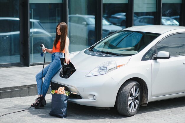 Öko-Elektroauto-Konzept Frau, die auf das Aufladen des Elektroautos wartet