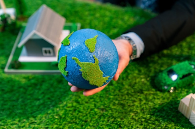Öko-Geschäft und  ⁇ Save Earth ⁇ -Konzept, gezeigt von einem Geschäftsmann oder CEO, der im Büro einen Papierglobus mit einem umweltfreundlichen Mockup hält, um die Reduzierung von CO2 und Kohlenstoffabdruck für eine grünere Zukunft zu fördern