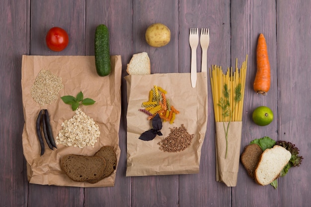 Öko-Taschen mit Produkten, die reich an komplexen Kohlenhydraten sind: Müsli, Brot, Nudeln und Gemüse auf Holztisch