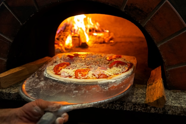 Foto koch aus dem hohen winkel, der pizza im holzofen backt