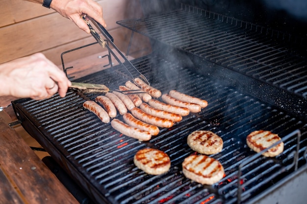 Koch bereitet Fleisch auf dem Grill während des Essensfests im Freien im Freien zu Imbisswagen-Brunch oder Catering-Event SchweinesteaksBayerische WürstchenBarbecue-Party Sommergrillparty oder Picknick im Hinterhof back