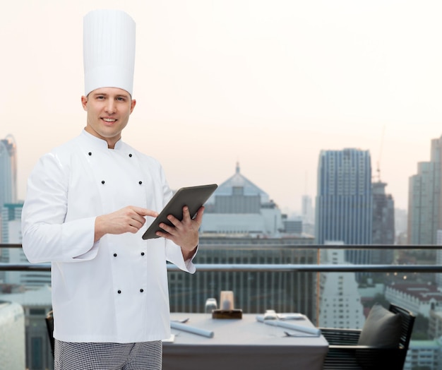 Koch-, Berufs- und Personenkonzept - glücklicher männlicher Chefkoch, der Tablet-PC-Computer über Stadtrestaurant-Lounge-Hintergrund hält