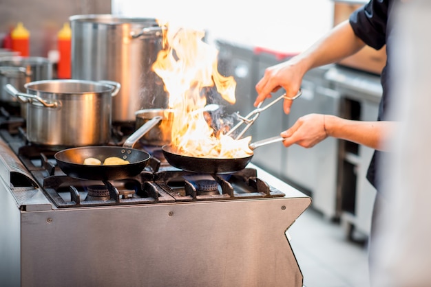 Koch braten Fleischsteak auf dem Gasherd mit Feuer in der Küche. Nahaufnahme auf die Bratpfanne