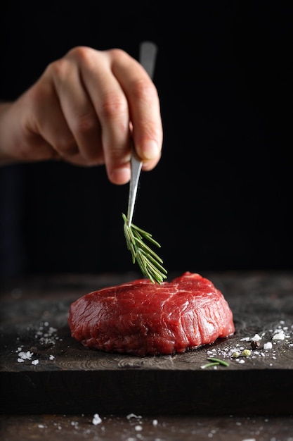 Koch, der frisches Fleisch an Bord kocht Dunkler Hintergrund Kochkonzept