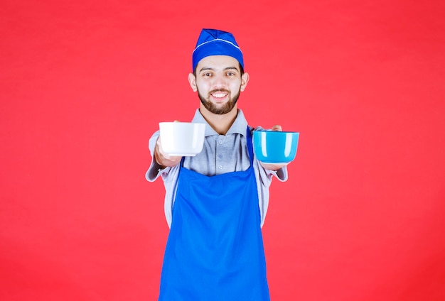 Koch in blauer Schürze, der blaue und weiße Keramikbecher in beiden Händen hält und dem Kunden serviert.