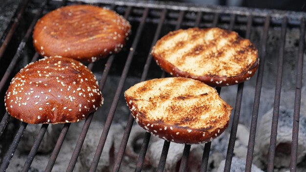 Koch in schwarzen Handschuhen macht und grillt Burgerbrötchen im Freien