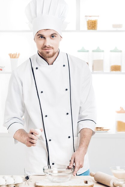 Koch in Uniform Breakseggs in Schüssel, um Teig in der Küche zuzubereiten