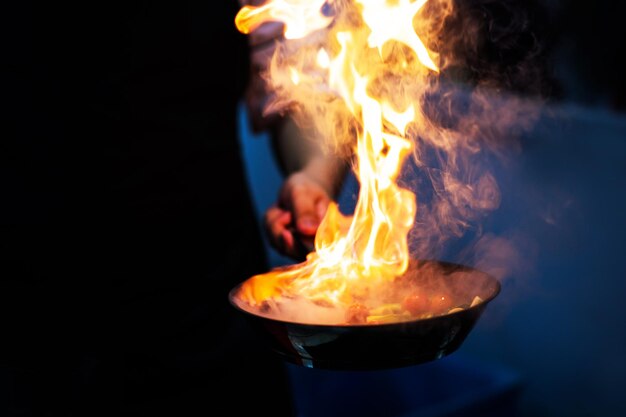 Koch kocht mit Flamme in einer Bratpfanne auf einem Küchenkochen