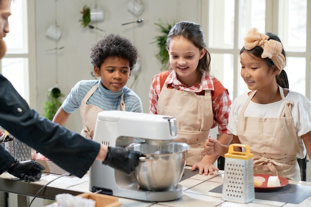 Koch macht Teig im Mixer und bringt Kindern das Kochen bei seiner Meisterklasse in der Küche bei