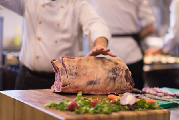 Koch mit Axt beim Schneiden eines großen Stücks Rindfleisch auf einem Holzbrett in der Restaurantküche