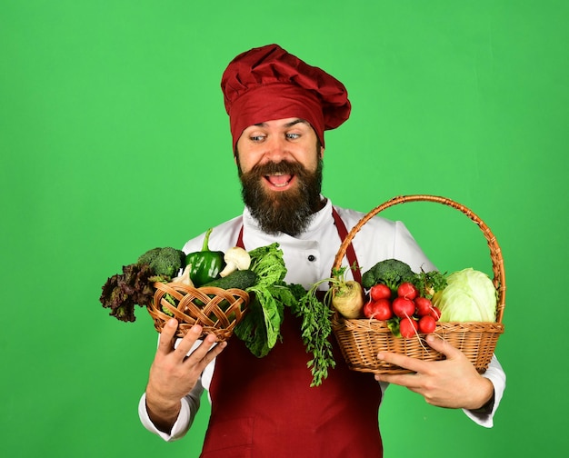 Koch mit fröhlichem Gesicht in Burgunder-Uniform hält Gemüse
