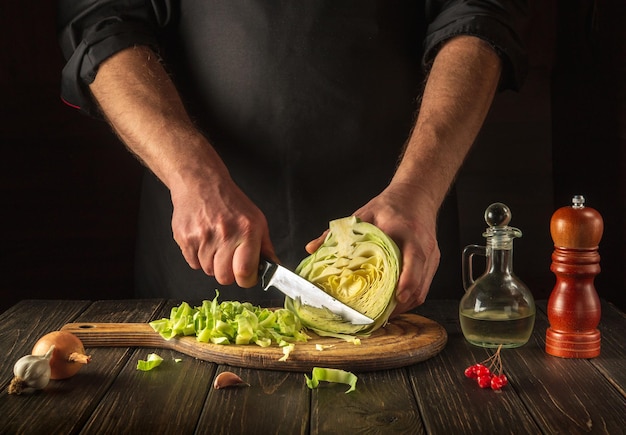 Koch oder Koch schneidet frischen Kohl mit Messer für Salat auf Vintage-Küchentisch mit frischem Gemüse