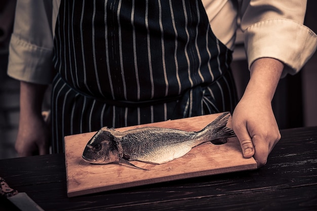 Koch schneidet den Fisch auf einem Brett