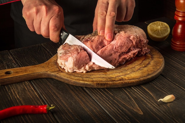 Koch schneidet Fleisch vor dem Backen mit einem Messer