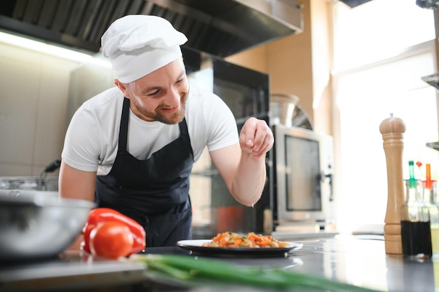 Koch schneidet Gemüse und Fleisch in Salz, konzentrierter Koch bereitet Essen vor, professioneller männlicher Koch, der gesundes Essen in einem kommerziellen Restaurant zubereitet.