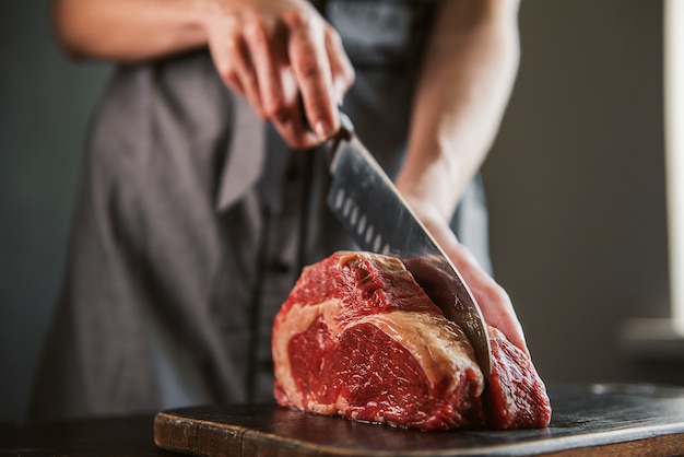 Koch schneidet rohes Fleisch für Steaks