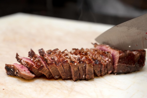 Koch schneidet saftiges Steak auf einem Brett in der gewerblichen Küche
